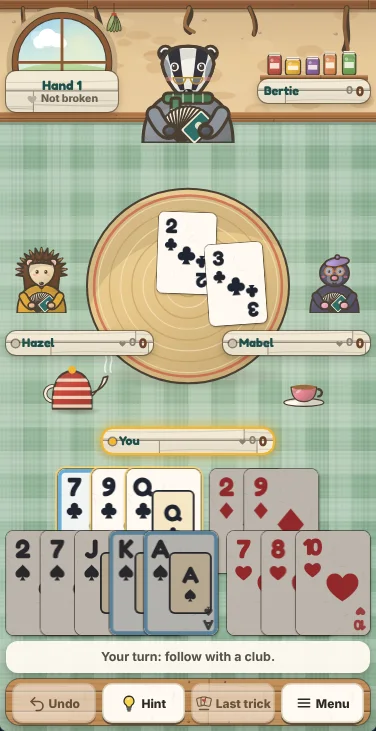 Actual Kettle Burrow Hearts gameplay on a phone held upright: Bertie the badger at the top of the burrow kitchen with the hand sign and his name plate on either side, Hazel the hedgehog and Mabel the mole at the sides with a trick on the woven mat between them, your thirteen cards in two overlapping rows sorted by suit with every rank showing, a message line and the Undo, Hint, Last trick and Menu buttons at the bottom.