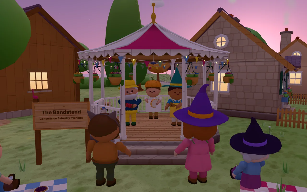 Actual CozyWorld Village screenshot: the band playing on the finished bandstand at dusk, with bunting and hanging baskets, residents in Halloween costumes dancing on the grass in front and sitting on picnic blankets.